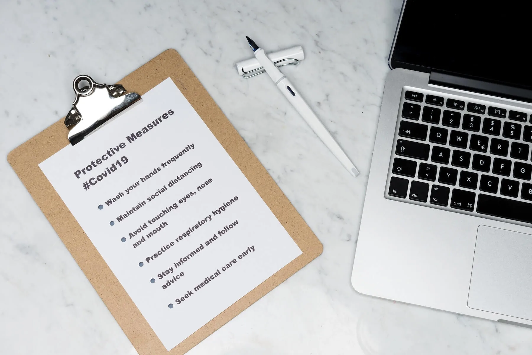 laptop and pen and clipboard with list of protective measures for covid19 on marble table nursing evidence based practice for nurses