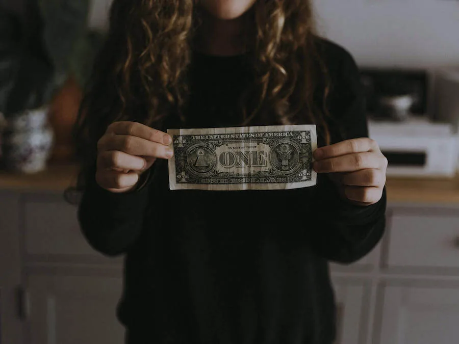 woman in black sweater holding dollar bill in front of her budgeting for nurses