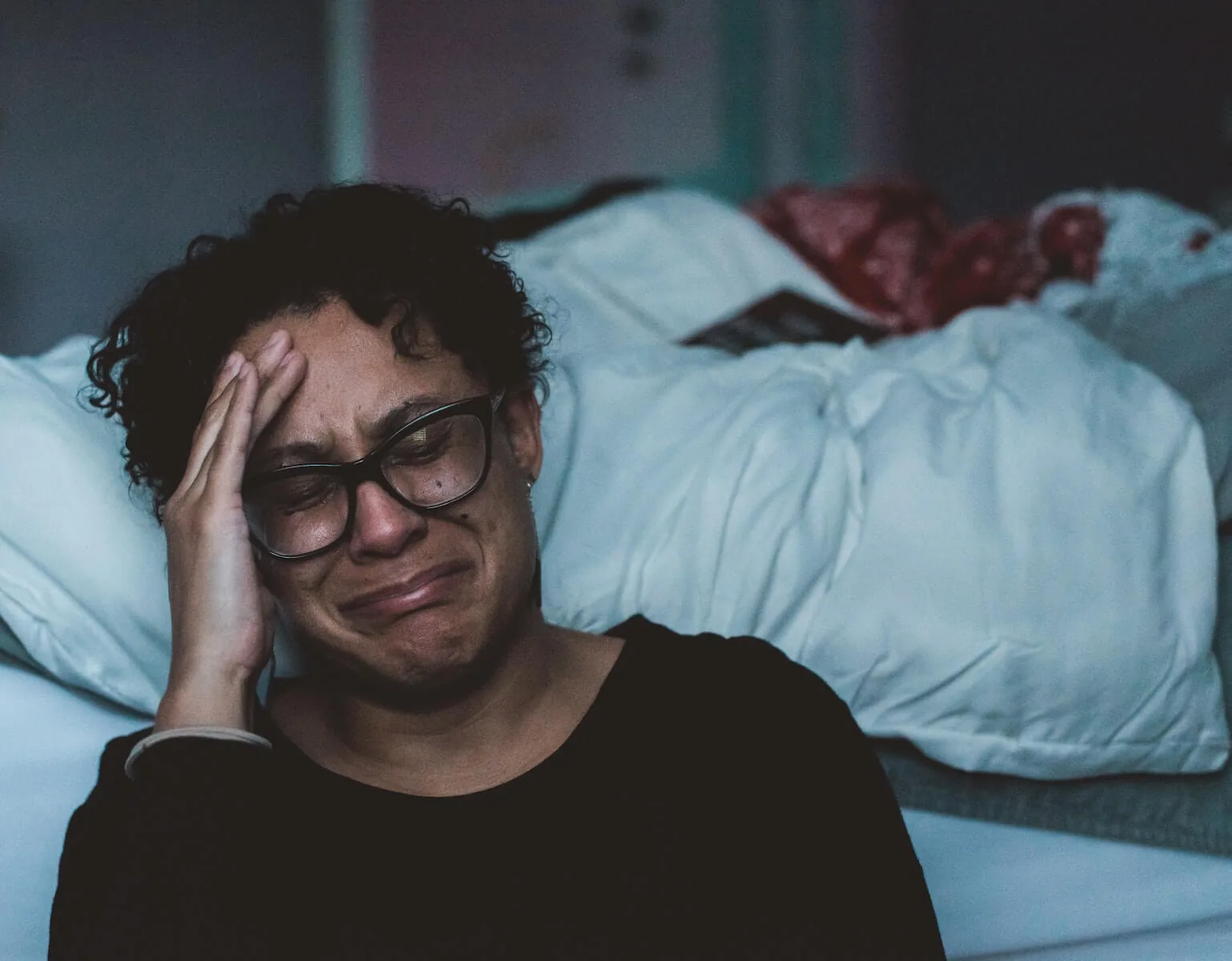 woman sitting in bedroom hand to face crying covid19 nursing moral injury