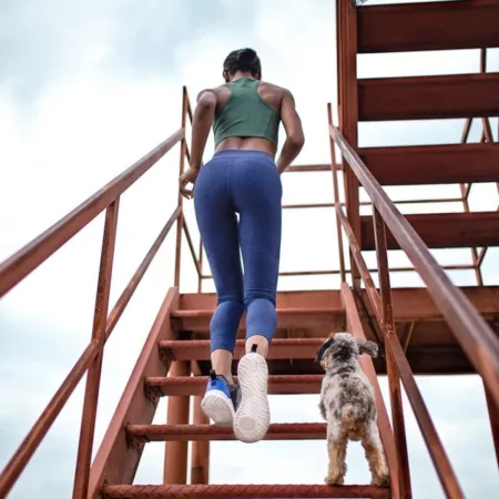 woman in athletic outdoor voices apparel running up metal staircase next to small dog