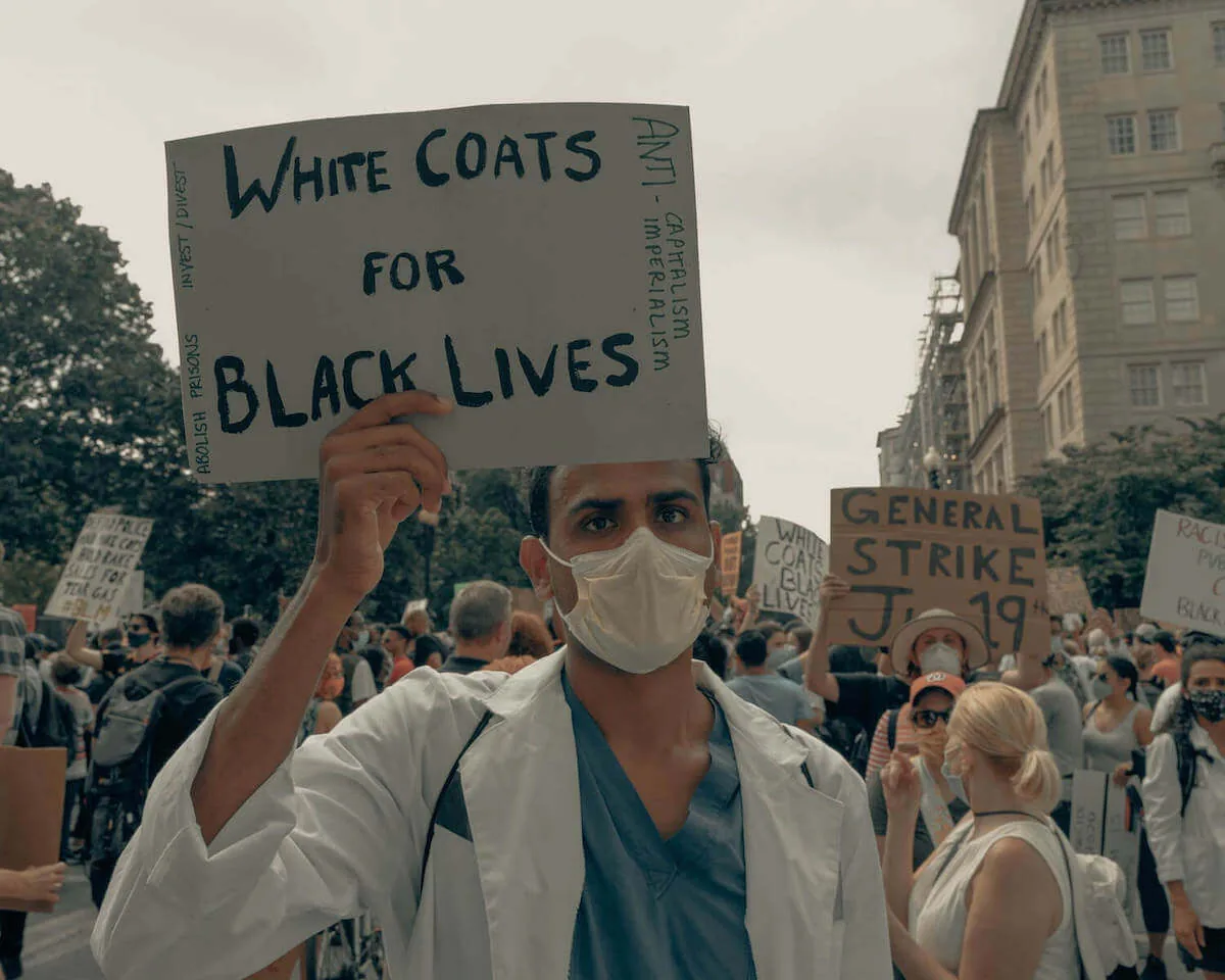 man at BLM protest holding white coats for black lives sign racial bias in healthcare healthcare disparity