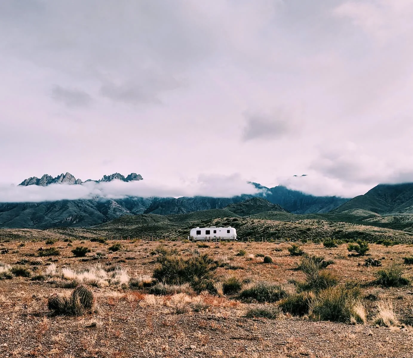 airstream RV on desertscape with mountains shrouded in clouds in the background travel nursing in an RV