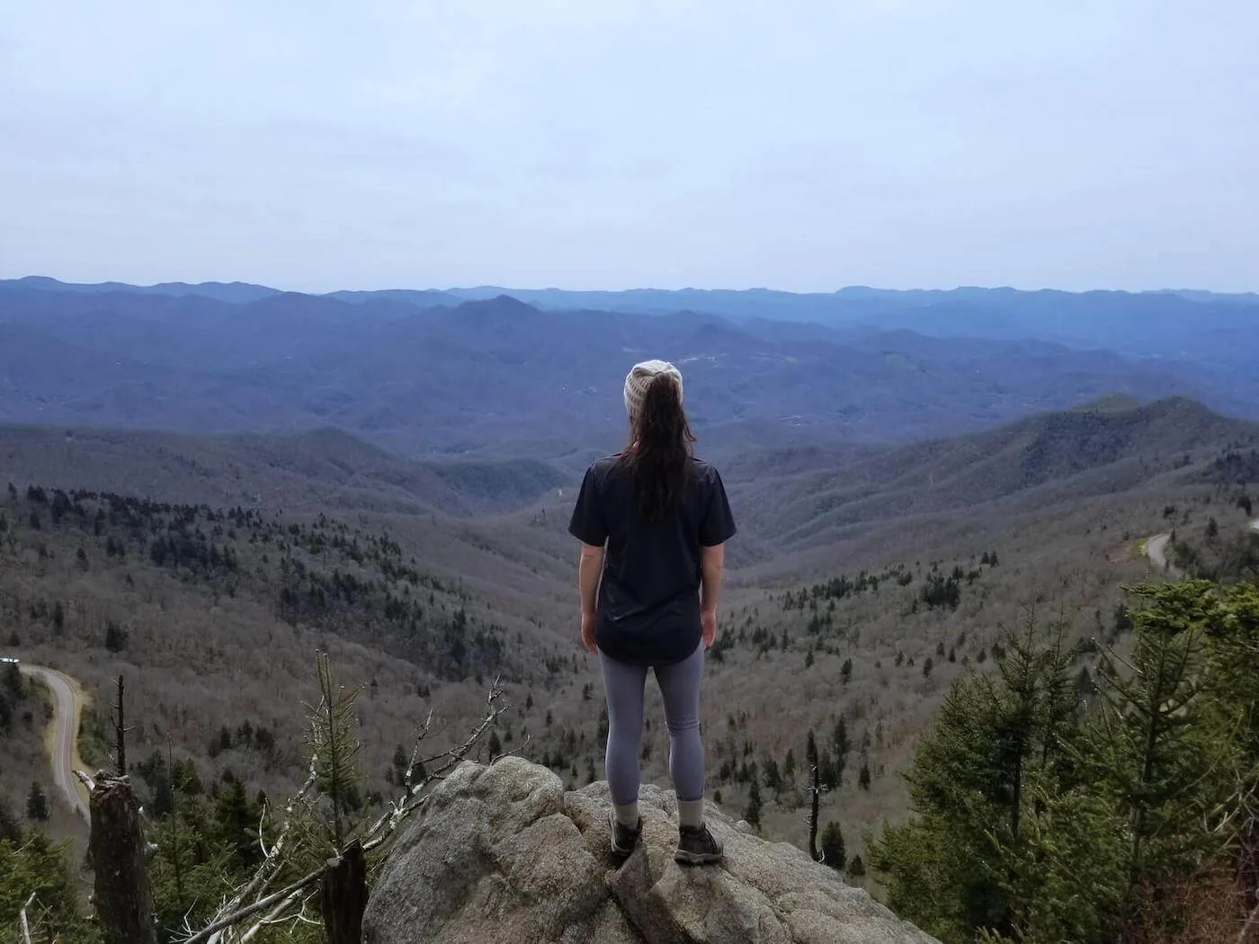 woman standing on cliff overlooking mountainous valley wilderness nursing