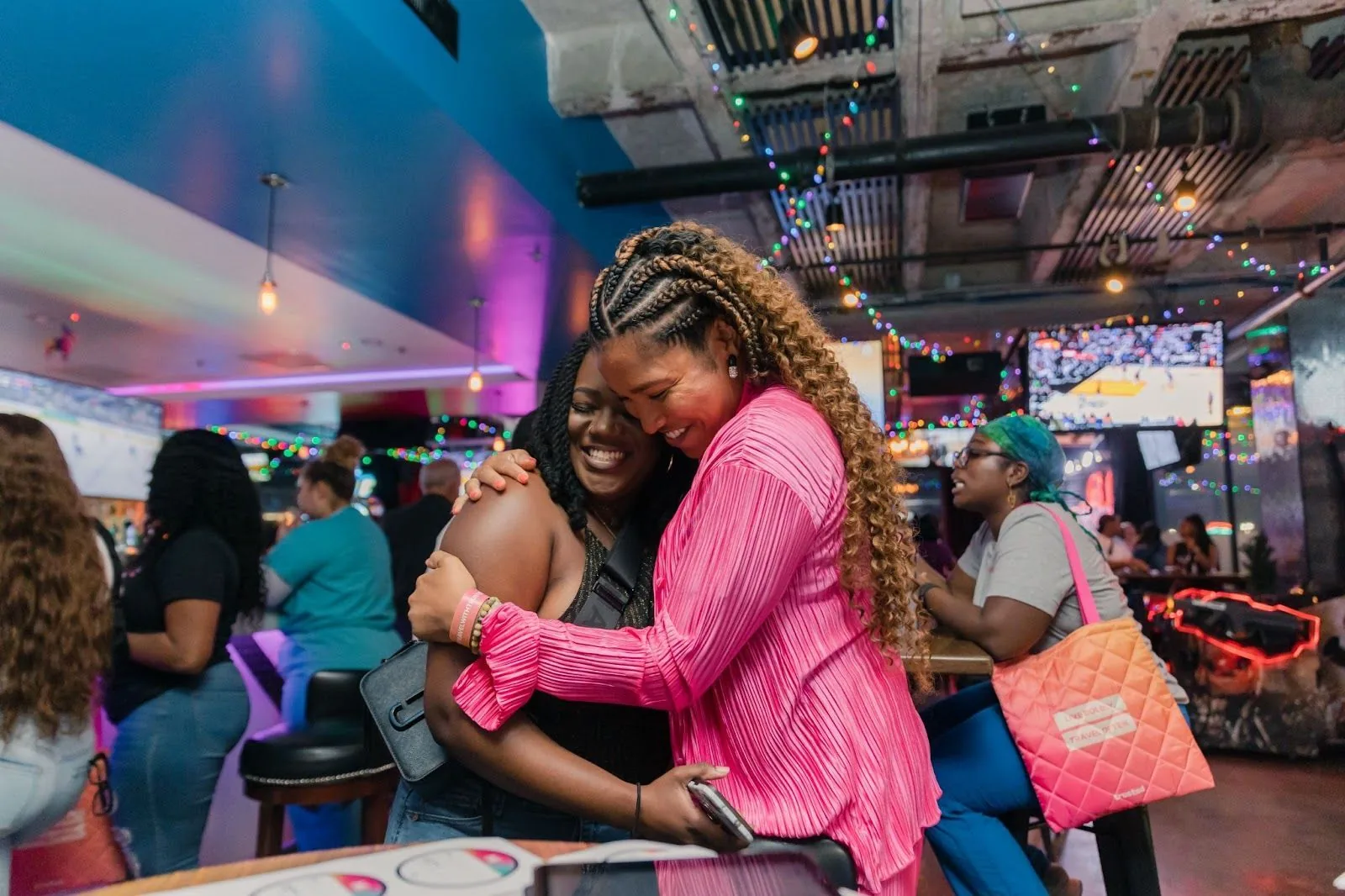 A heartfelt embrace between two women at a vibrant social event, surrounded by others in a lively setting with colorful lights, symbolizing the camaraderie and support found within the Trusted Health community.
