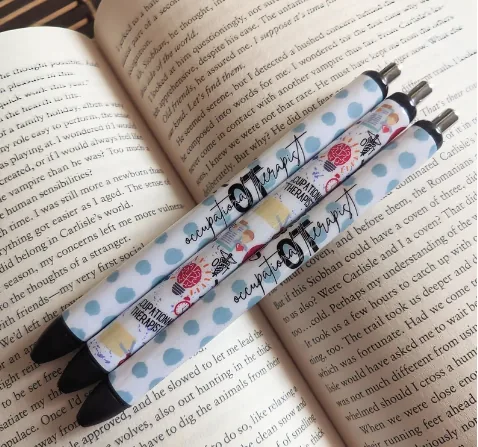 Two custom-designed epoxy gel pens resting on an open book, featuring blue and white polka dots and a pattern of anatomical hearts and ‘Occupational Therapy’ script. These pens provide a personalized and stylish touch for any occupational therapist’s daily notes.