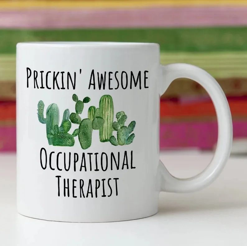 A white coffee mug with the playful phrase 'Prickin' Awesome Occupational Therapist' printed above a vibrant illustration of various green cacti. This unique mug is sure to bring a touch of humor and pride to any occupational therapist's morning routine.