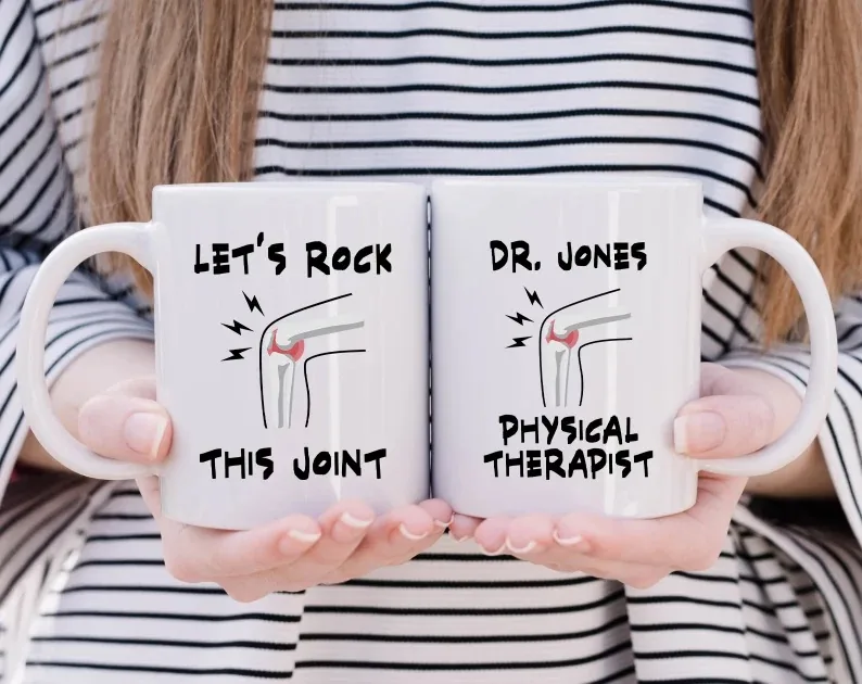 A person holds two white mugs, each featuring an illustration of a knee joint with musical notes and the phrase 'Let's Rock This Joint'. One mug is personalized with 'Dr. Jones Physical Therapist'. These mugs add a humorous and personalized touch to any physical therapist's coffee break