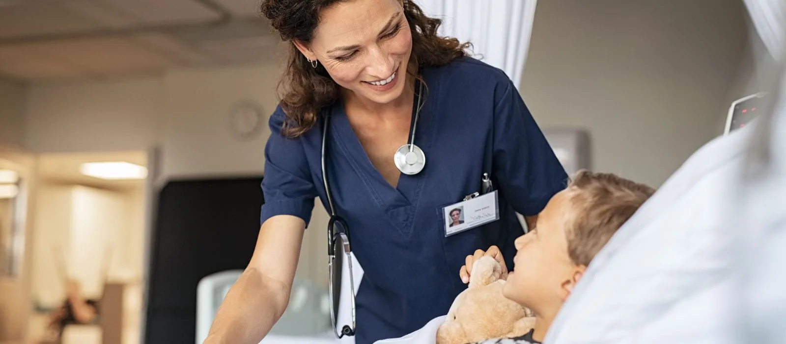 A pediatric nurse comforts a young patient holding a teddy bear in a hospital bed, highlighting the nurturing environment of the pediatric care unit.
