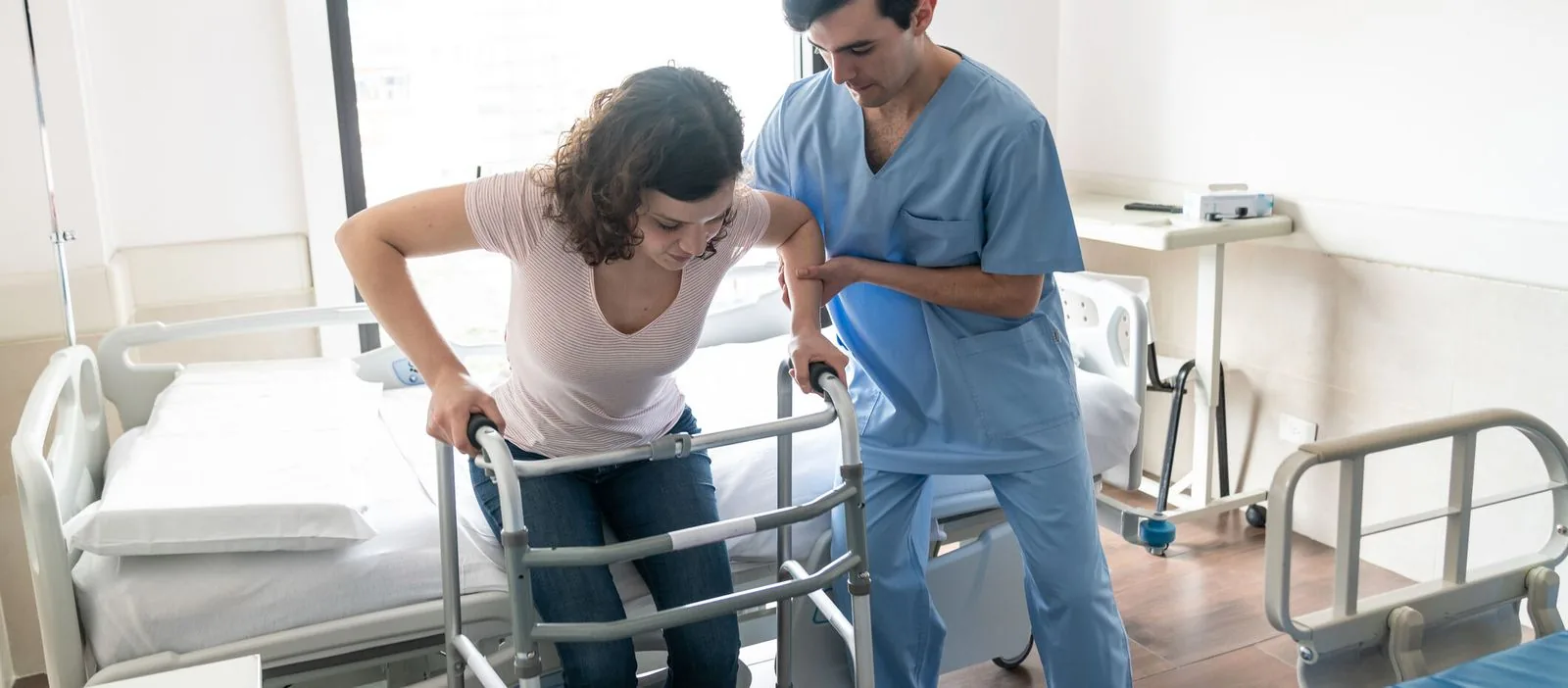 "A patient in a rehabilitation unit is assisted by a healthcare professional in blue scrubs, using a walker to aid in mobility. This moment captures the crucial support provided in rehab units to help patients regain independence.