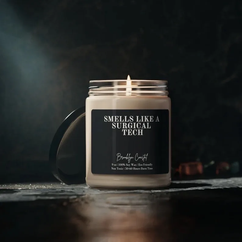 A lit soy wax candle in a sleek black jar labeled 'SMELLS LIKE A SURGICAL TECH', with eco-friendly and non-toxic features, designed to bring warmth and humor to a surgical tech's home.