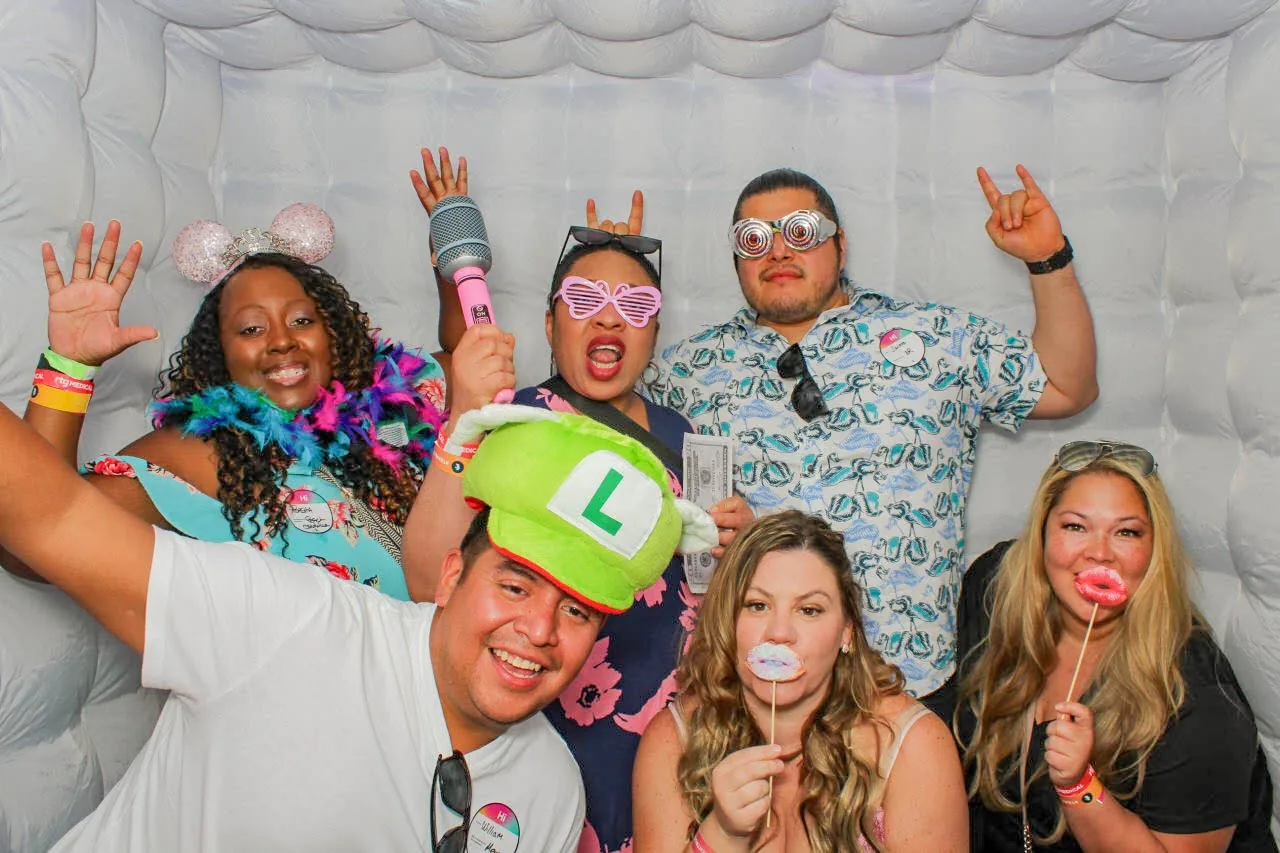 A group of six exuberant people in a photo booth with props, expressing joy and excitement, symbolizing the festive spirit of the Trusted Community's Nurses Week events across various cities.