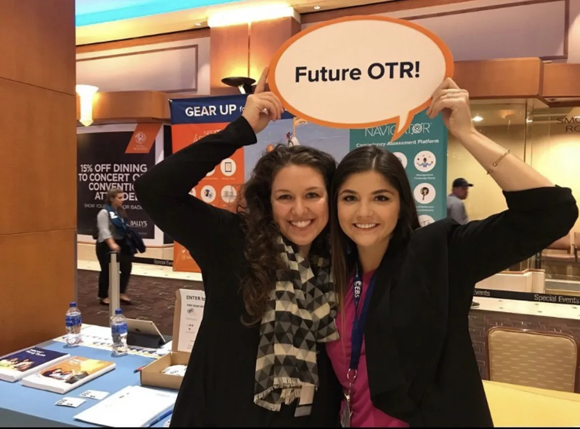 At a professional event, the author is joyfully raising a sign above her head that declares 'Future OTR!', alongside a supportive friend.