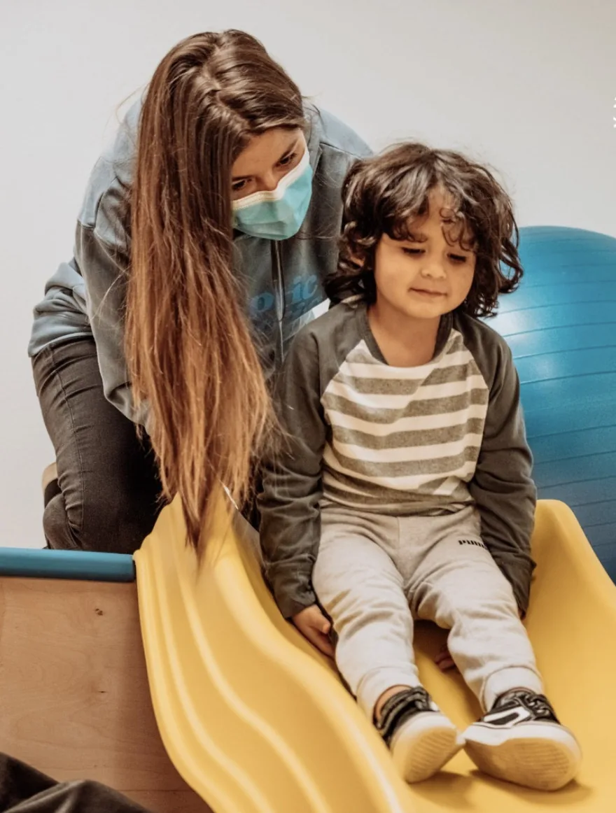 The author is assisting a young child on a slide in a pediatric therapy session.